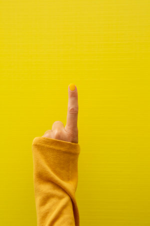 Vertical photograph of a woman's finger with yellow fingernail pointing upwards on a yellow background.の写真素材