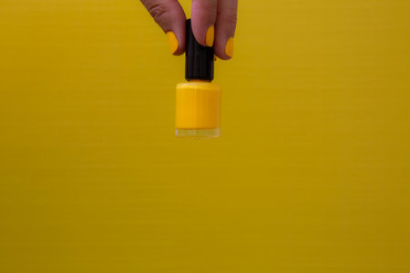 Horizontal photograph of a woman's hand with yellow nails holding a bottle of yellow nail polish on a yellow background.の写真素材