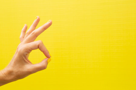 Horizontal photograph of a woman's hand with her nails painted yellow, giving a thumbs-up gesture.の写真素材