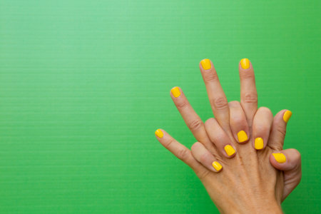 Horizontal photograph of a woman's hands clasped tightly with her nails painted yellow on a green backgroundの写真素材