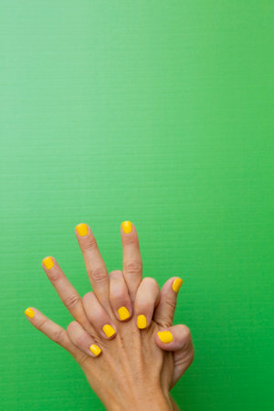 Vertical photograph of a woman's hands clasped tightly with her nails painted yellow on a green background.の写真素材