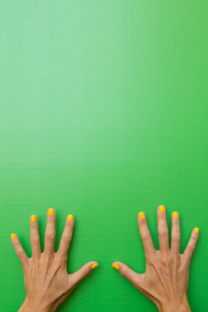 Vertical photograph of a woman showing her ten fingers with her nails painted yellow on a green background.の写真素材