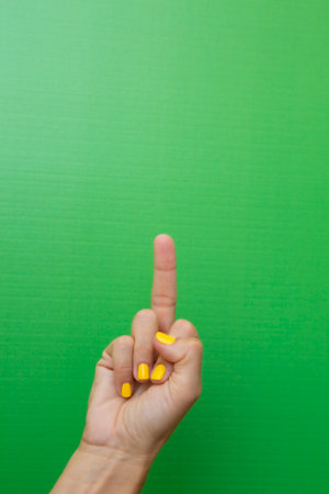 Finger of a woman with her fingernails painted yellow on a green background.の写真素材