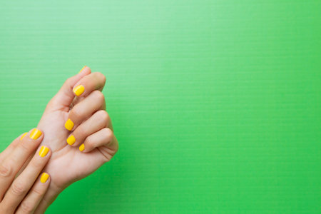 Horizontal photograph of a woman holding both hands with her nails painted yellow on a green background.の写真素材