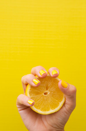 Hand of a woman with yellow fingernails holding half a lemon with yellow backgroundの写真素材