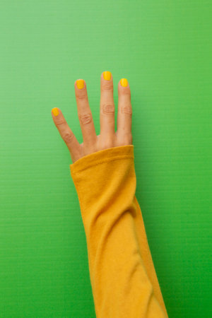 Four fingers of a 45-year-old woman with her nails painted yellow on a green background.の写真素材
