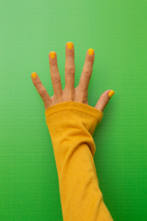 Five fingers with yellow-painted nails on a green background.の写真素材