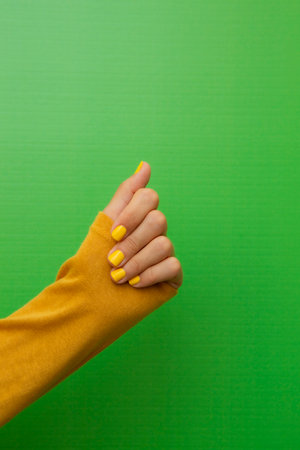 Hand of a woman with yellow fingernails on a green background.の写真素材