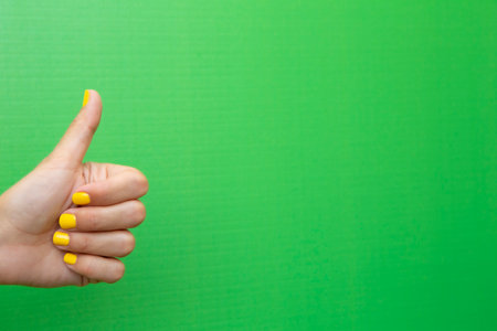 A woman's middle finger showing it as a sign of approval with her fingernails painted yellow on a green background.の写真素材