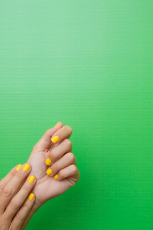Vertical photograph of a woman holding both hands with her nails painted yellow on a green background.の写真素材