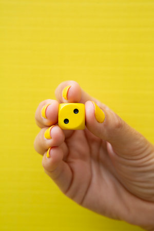 Woman's hand holding a dice with her fingers on a yellow background.の写真素材