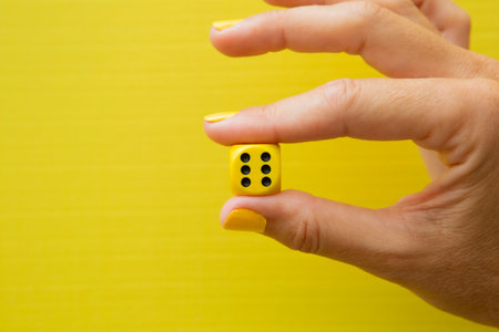 Woman's hand holding a yellow die with the number six on it with the yellow background