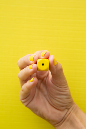 Woman's hand holding a dice with her fingers on a yellow background.の写真素材