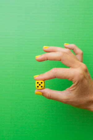 Woman's hand holding a yellow die with the number five on it with the green backgroundの写真素材