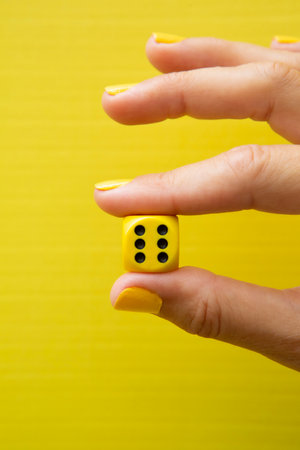 Woman's hand holding a dice with her fingers on a yellow background.の写真素材