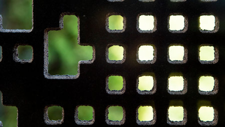 Metal surface with a mosaic of squares and rectangles in backlight and with the green background of the trees out of focus.の写真素材