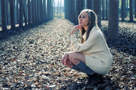 Beautiful blonde girl, dressed with a beige dress, standing in a poplar forestの写真素材