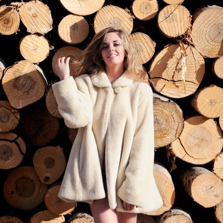 Portrait of a beautiful blonde woman wearing a white coat on poplar trunksの写真素材