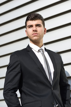 Young businessman near a modern office building wearing black suit and tie. Man with blue eyesの写真素材