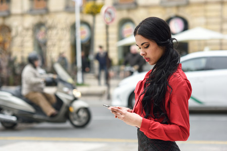 Portrait of hispanic bussinesswoman in urban background looking at her mobile phoneの写真素材
