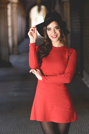 Portrait of young woman, model of fashion, smiling in urban background wearing red dress and hatの写真素材