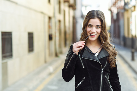 Portrait of young woman smiling in urban background wearing casual clothes with modern sunglasses. Girl with long curly hairの写真素材
