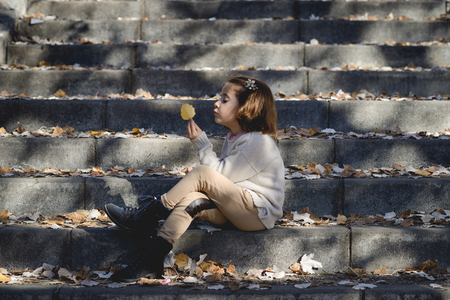 Little girl playing in a city park in autumn, wearing pants and jersey with a hairpin in hairの写真素材