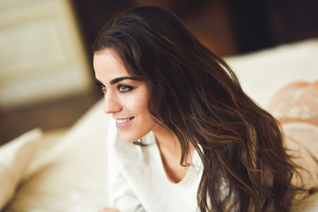 Sexy young smiling woman in lingerie posing on the bed. Brunette girl with white panties and pyjama in her bedroomの写真素材