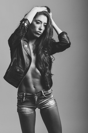Beautiful woman body in denim jeans shorts and black leather jacket. Black and white studio shot.の写真素材