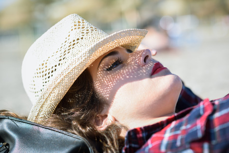 Close-up of young woman resting on the beach with plaid shirt and sun hatの写真素材