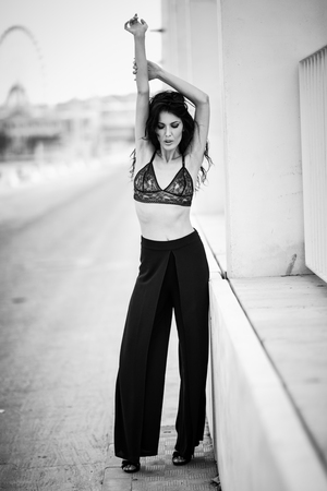 Brunette girl, model of fashion, wearing black bra and trousers in urban background. Young woman with long curly hairstyle.の写真素材