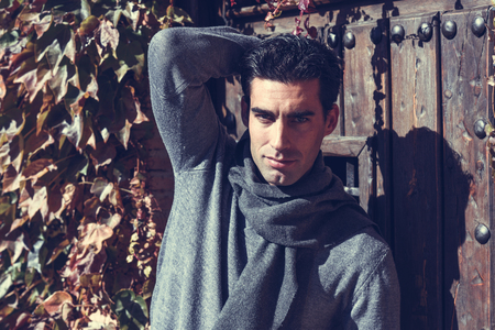 Handsome man wearing winter clothes in autumn leaves background. Young male with swater and scarf.の写真素材