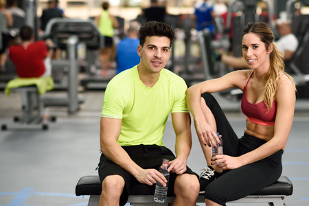 Handsome man and beautiful sporty woman drinking water after workout in the gymの写真素材