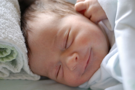 Newborn baby girl in hostpital bed sleeping and smiling. Caucasian female.の写真素材