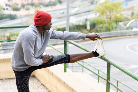 Black man doing stretching before running outdoors. Young male exercising with city scape at the background.の写真素材