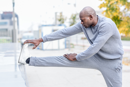 Black man doing stretching before running in urban background. Young male exercisingの写真素材
