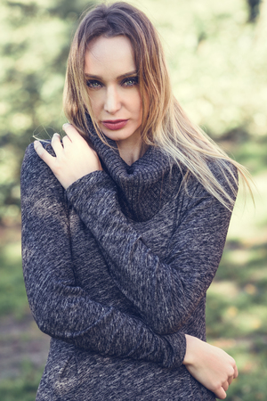 Young blonde woman standing in a park with autumn colors. Beautiful girl wearing winter dress. Female with straight hair and blue eyes.の写真素材