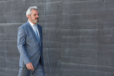 Senior businessman walking outside of modern office building. Successful business man wearing suit and tie in urban background.の写真素材