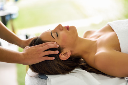 Young caucasian smiling woman receiving a head massage in a spa center with eyes closed. Female...