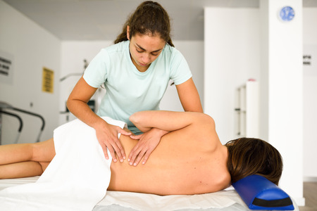 Professional female physiotherapist giving lumbar shoulder massage to brunette woman in hospital....