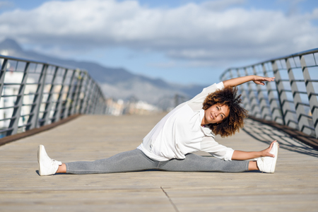 Young black woman doing stretching after running outdoors. Girl exercising with city scape at the background. Afro hair.の写真素材