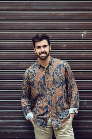 Young smiling man, model of fashion, wearing modern shirt in the street. Guy with beard and modern hairstyle in urban background.の写真素材
