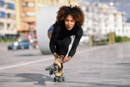 Young fit black woman on roller skates riding outdoors on urban street. Smiling girl with afro hairstyle rollerblading on sunny dayの写真素材