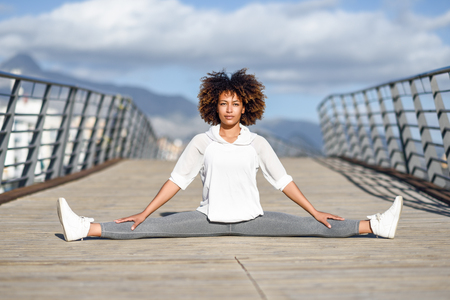 Young black woman doing stretching after running outdoors. Girl exercising with city scape at the background. Afro hair.の写真素材