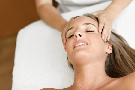 Young blond woman receiving a head massage in a spa center with eyes closed. Female patient is receiving treatment by professional therapist.の写真素材