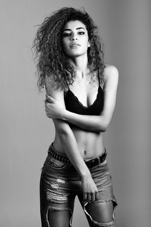 Beautiful young woman with black curly hairstyle. Girl wearing black bra and blue jeans.の写真素材