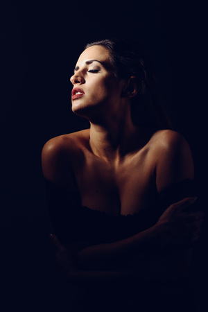 Young brunette woman in black lingerie in chiaroscuro lighting. Attractive girl, model of fashion. Studio shot.の写真素材
