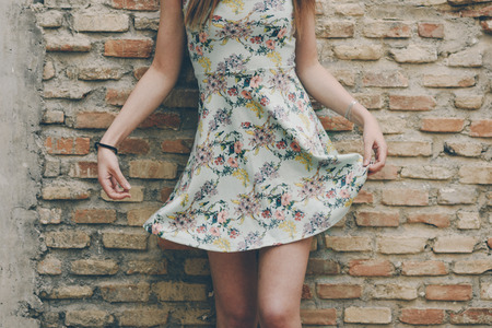Sexy unrecognizable woman raising her dress on brick wall.