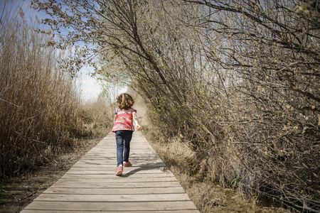 Little girl walking on a path of wooden boards in a wetland in Padul, Granada, Andalusia, Spainの写真素材