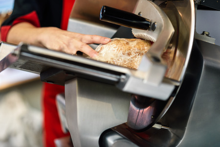 Close-up of female butcher cutting york ham in a cutting machine inside a butcher shop.の写真素材